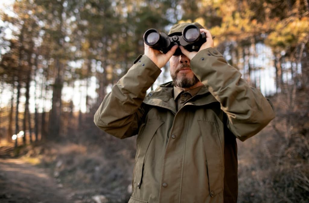 A man in a forest using binoculars to look into the distance
