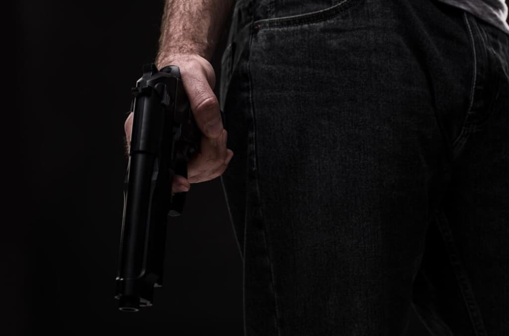 Person holding a handgun by their side against a dark background