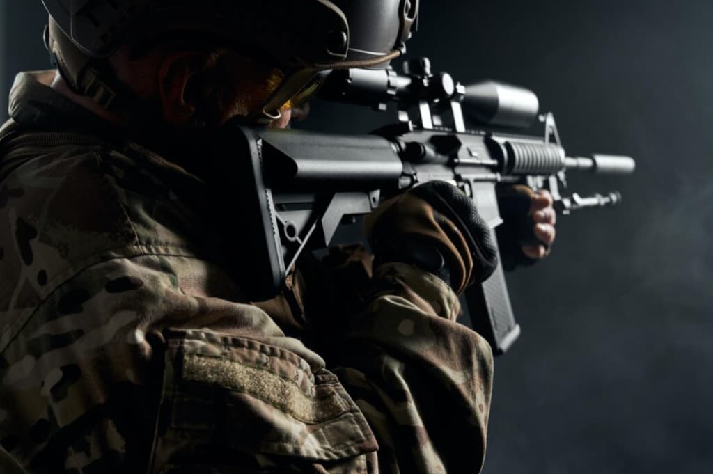 Soldier in camouflage gear aims a tactical rifle, highlighted against a shadowy background