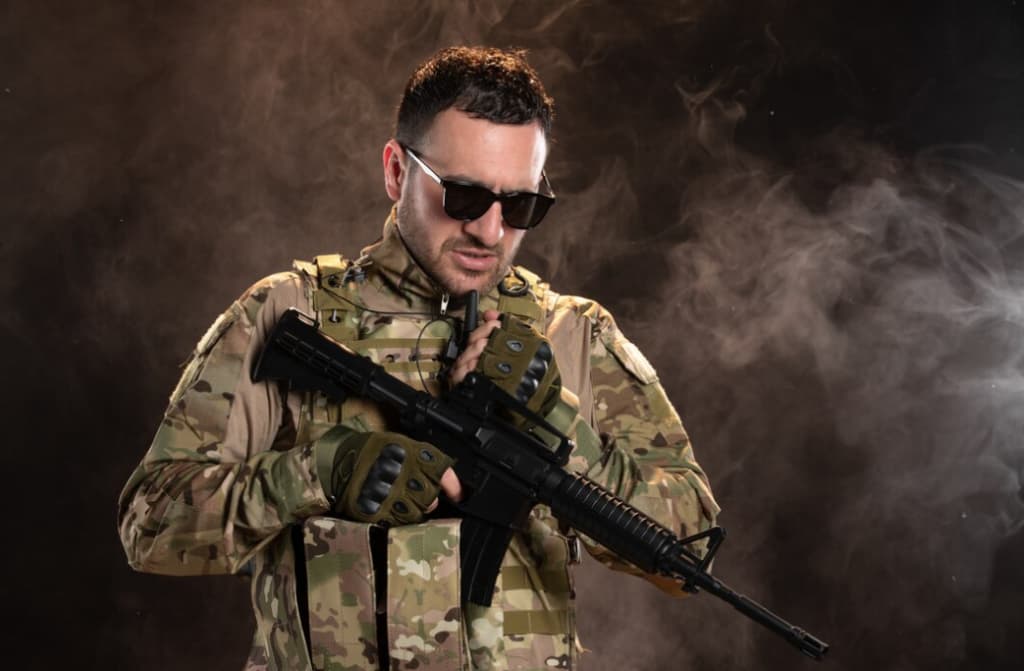 A man in camouflage and sunglasses holds a rifle with smoke around