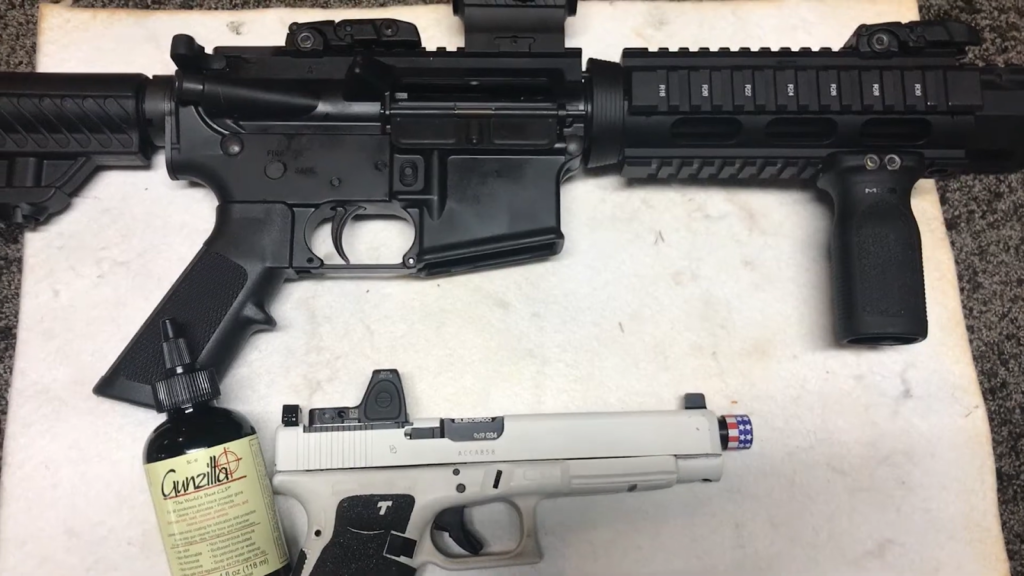 Two disassembled guns and a bottle of Gunzilla CLP on a table